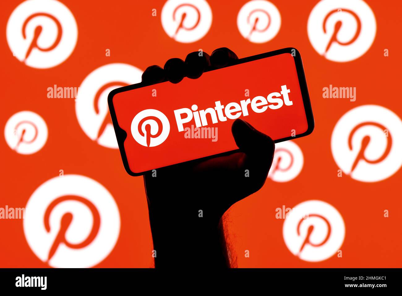 Smartphone mit Pinterest Social-Media-Service-Logo auf dem Bildschirm in geballter Hand auf dem Hintergrund der Pinterest-Logos Stockfoto