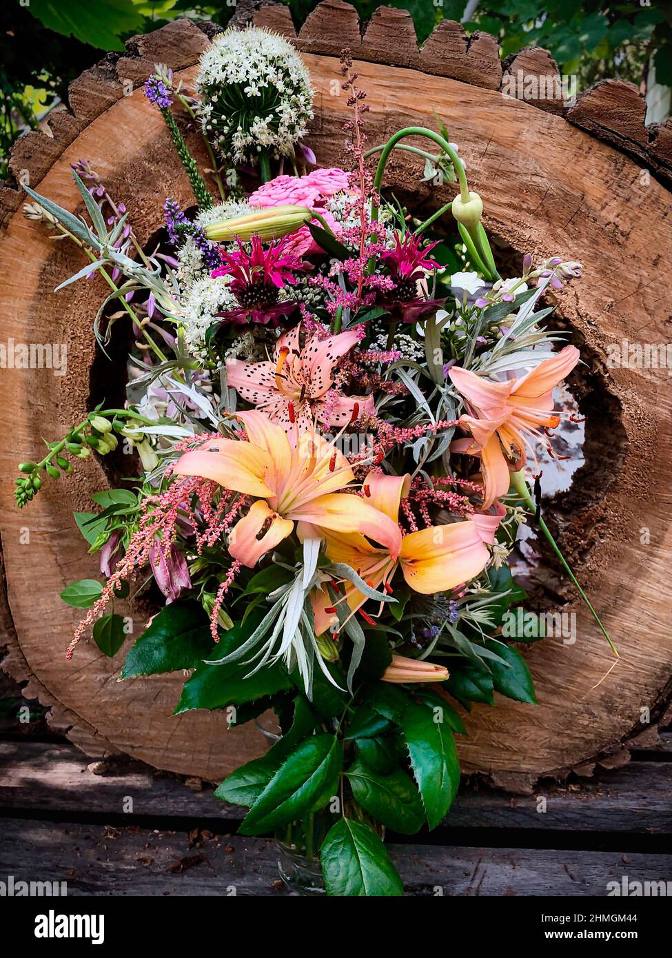 Romantischer Strauß in einer Vase, die aus altem Baum geschnitten wurde. Die Zusammensetzung umfasst Lilie, Fuchshandschuh, Allium, Astilbe, Monarden, rosen, veronica, Knoblauchpfeile, Wurmw Stockfoto