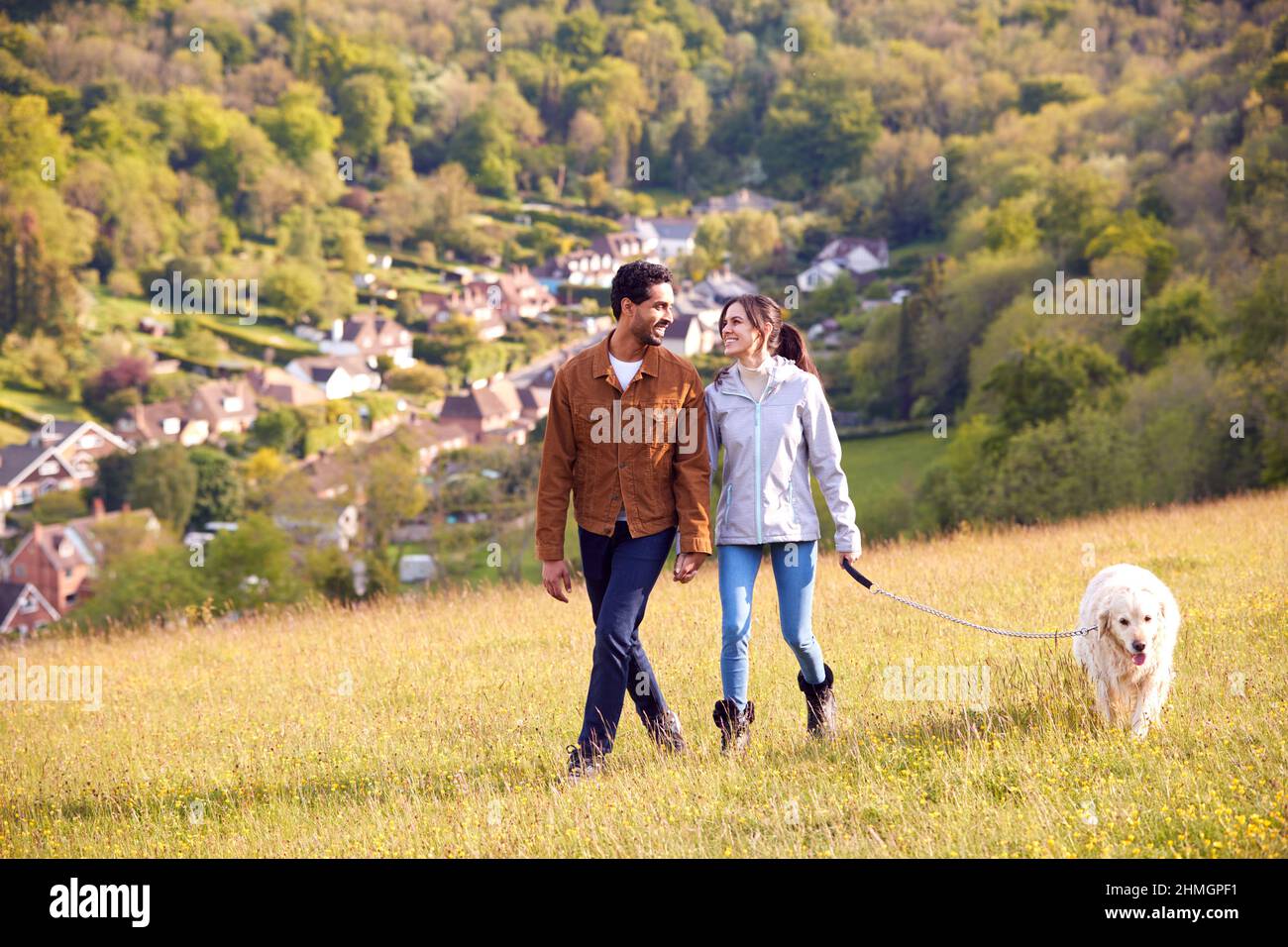 Paar Mit Pet Golden Retriever Hund Zu Fuß Entlang Pfad Über Feld In Der Landschaft Stockfoto