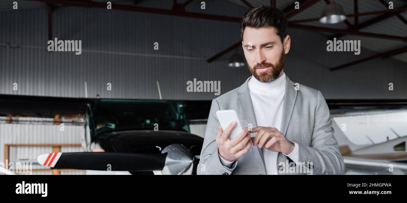 Bärtiger Mann im Anzug mit Smartphone in der Nähe von modernen Hubschrauber, Banner Stockfoto