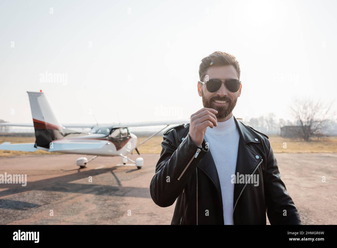 Zufrieden Pilot in schwarzer Lederjacke und Sonnenbrille in der Nähe Hubschrauber Stockfoto