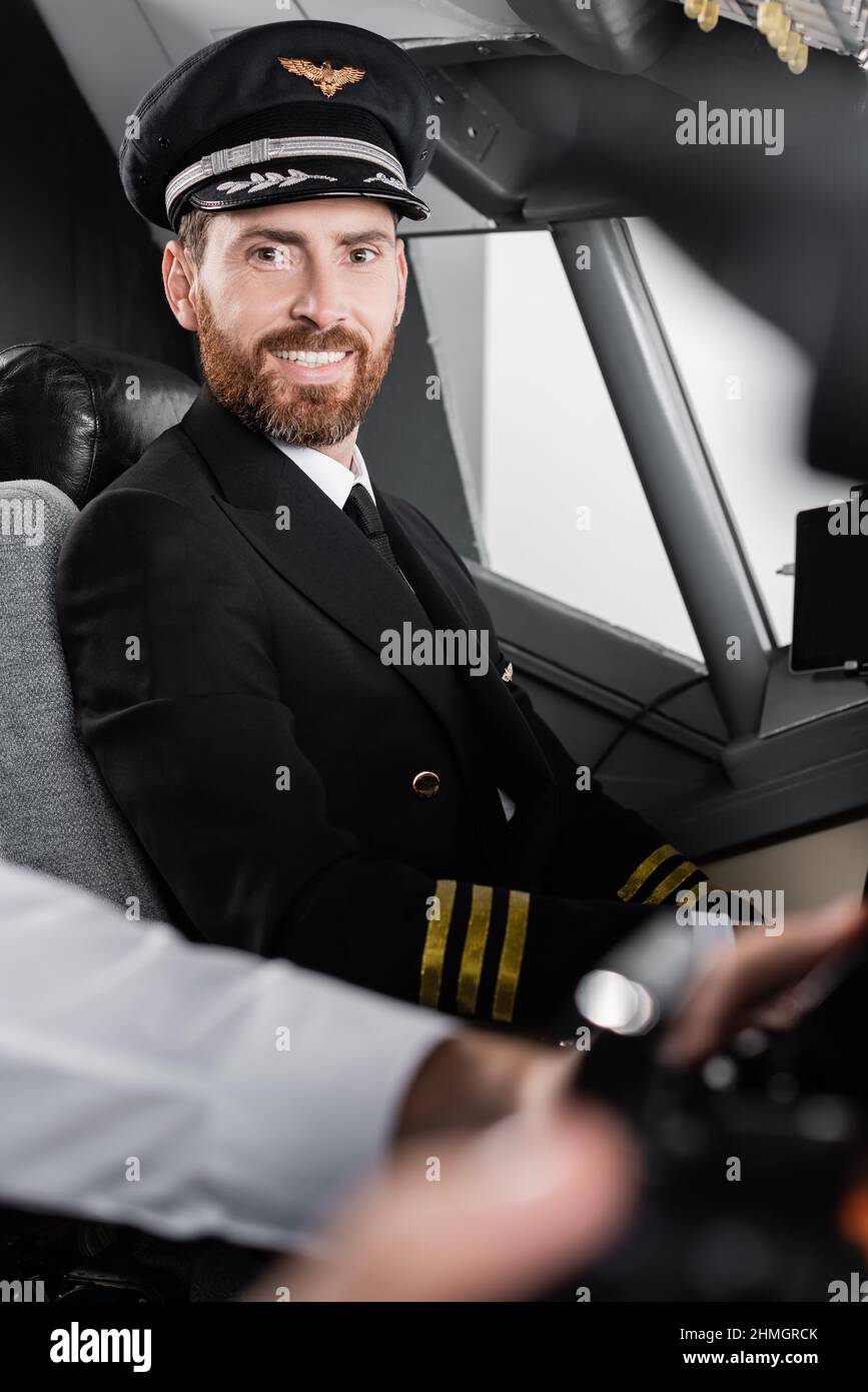 Bärtiger Pilot in Uniform und Mütze lächelnd fast verschwommener Co-Pilot Stockfoto