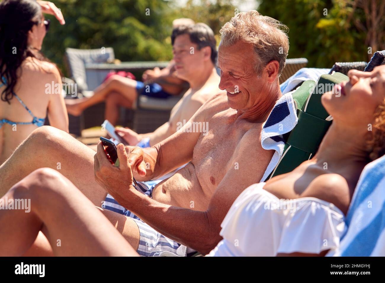 Älterer Mann, Der Im Sommerurlaub Mit Dem Mobiltelefon Unterwegs Ist, Um Sich Auf Der Sonnenliege Am Außenpool Zu Entspannen Stockfoto