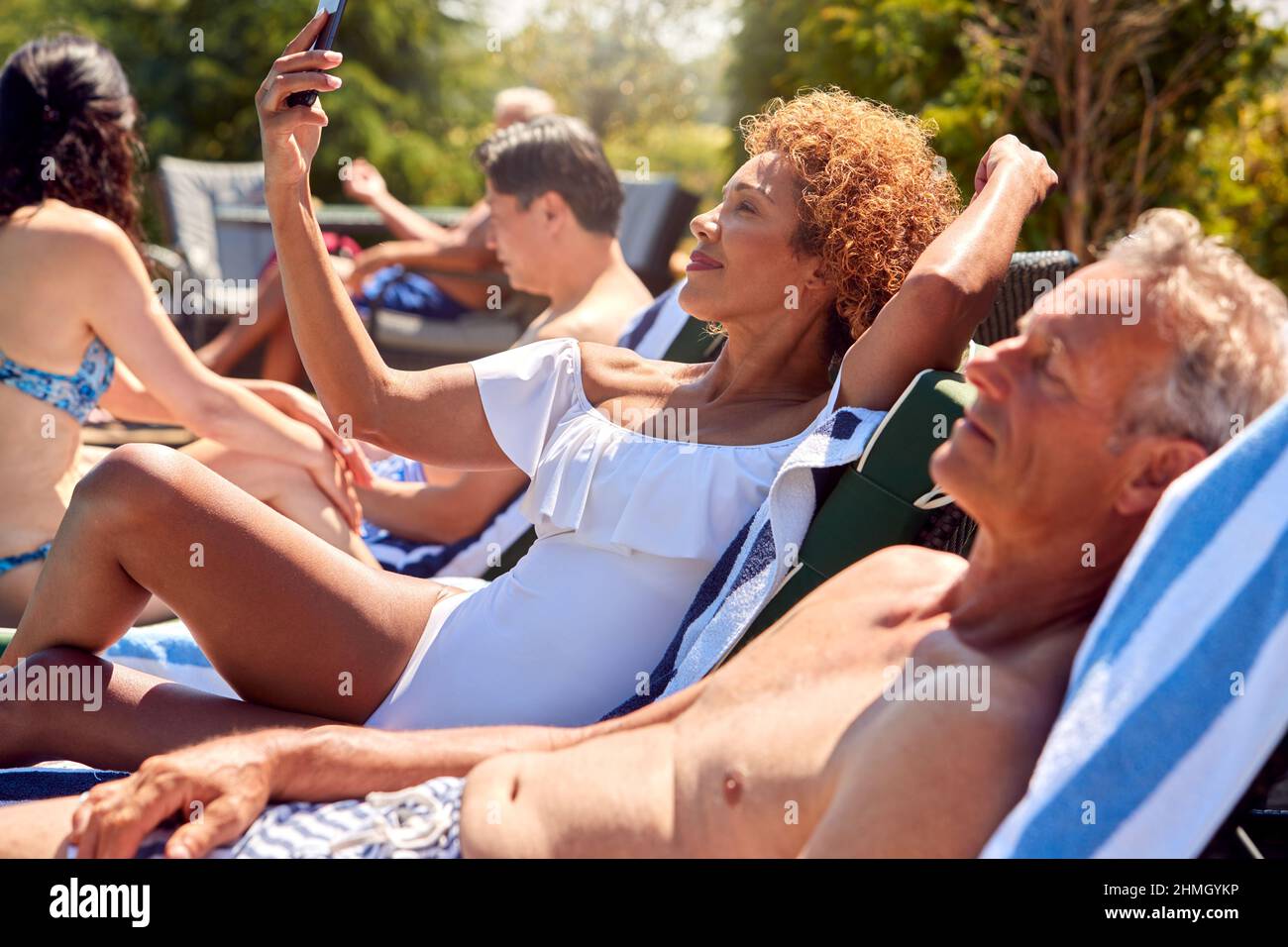 Ältere Frau, Die Im Sommerurlaub Mit Dem Mobiltelefon Unterwegs Ist, Um Sich Auf Der Sonnenliege Am Außenpool Zu Entspannen Stockfoto