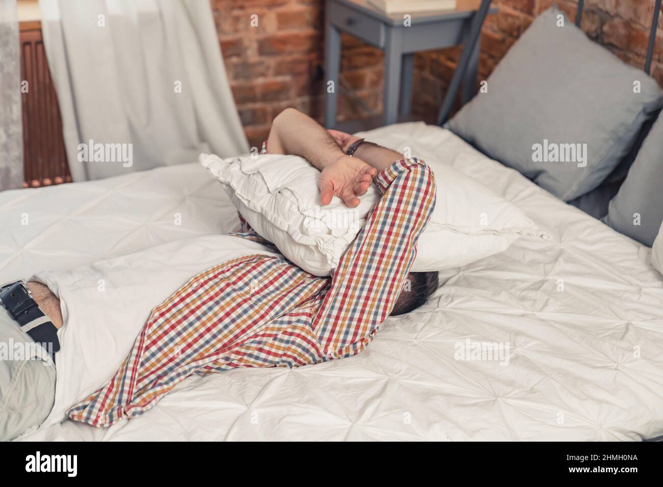 Müder kaukasischer Mann legte sich auf sein Bett und bedeckte sein Gesicht mit einem weißen Kissen. Hochwertige Fotos Stockfoto