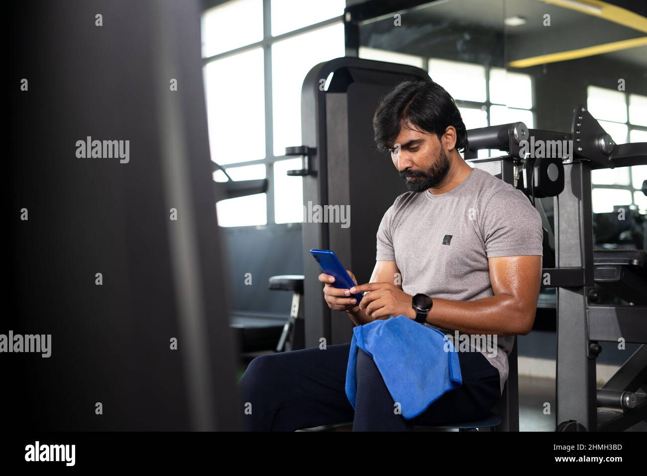 Junger indischer Mann überwacht oder verfolgt Kalorien mit Handy-Applikation im Fitnessstudio - Konzept der Technologie, Überprüfung Trainingspläne und Wellness Stockfoto