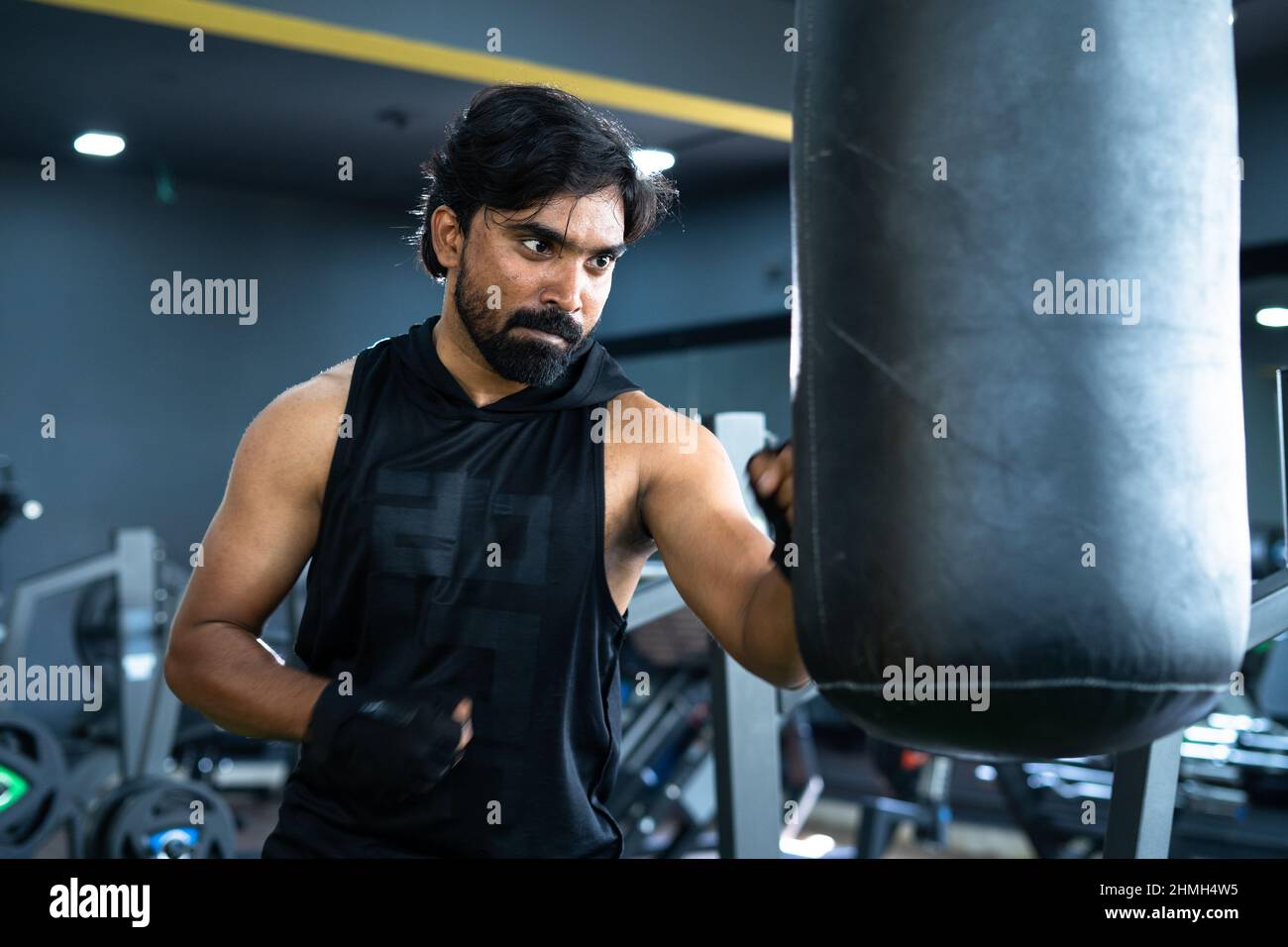 Wütender junger indischer Athlet, der Boxsack im Fitnessstudio boxt - Konzept von motivationalem, fleißigen, Kampf- und Workout-Training Stockfoto