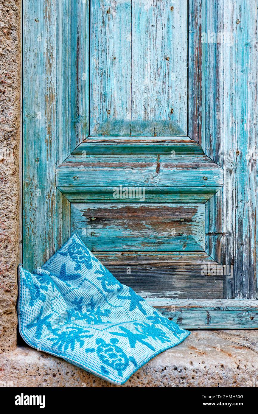 Blaue Holztür mit verwitterter Farbe, davor befindet sich ein Sitzkissen Stockfoto