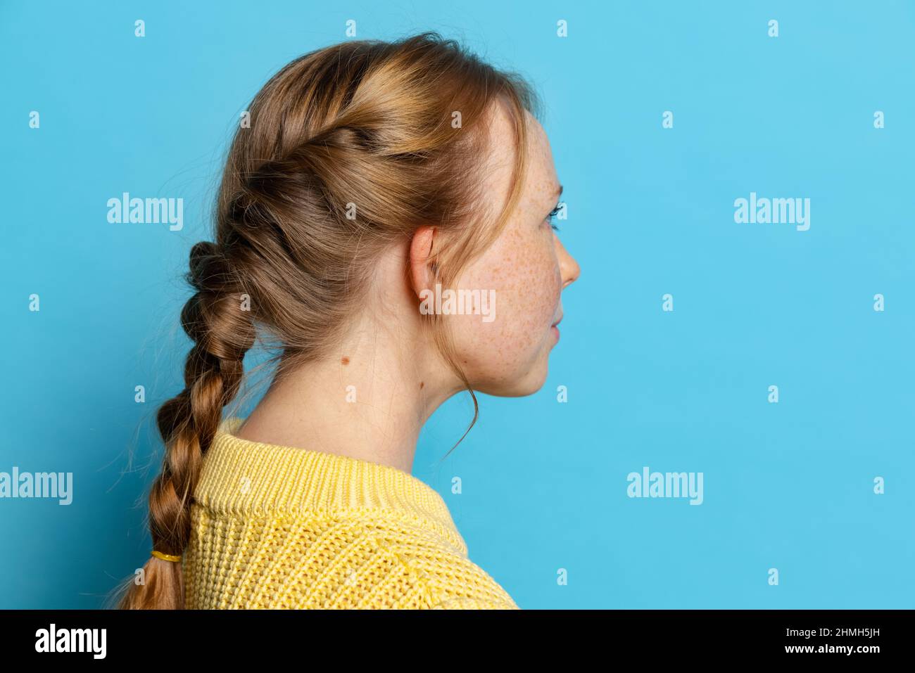 Profilansicht des jungen Mädchens in gelbem Pullover posiert isoliert auf blauem Hintergrund. Konzept der Emotionen, Mimik Stockfoto