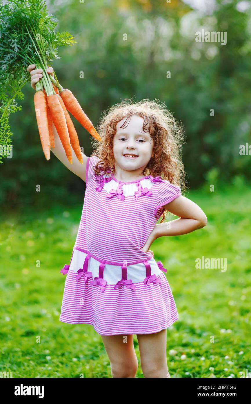 Kleines Mädchen mit gelber Karotte im Garten. Stockfoto