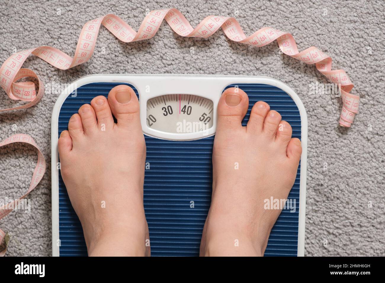 Damenfüße auf Bodenschuppen, Draufsicht. 30 oder 40 Kilogramm auf einer Skala, die Idee von Anorexie und Essstörungen Stockfoto