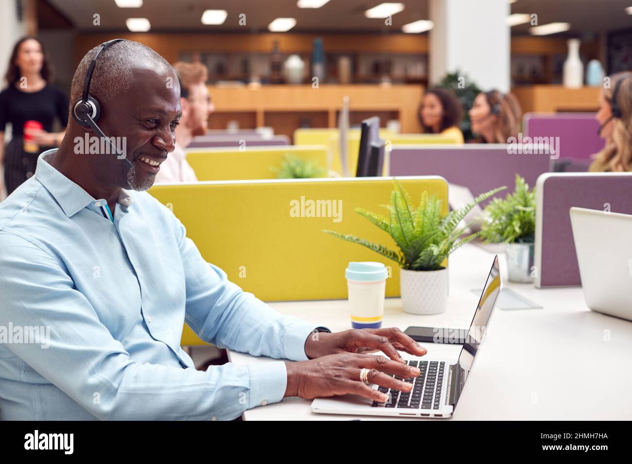 Ein Reifer Geschäftsmann, Der Ein Telefon-Headset Trägt, Spricht Mit Dem Anrufer Im Geschäftigen Kundencenter Stockfoto