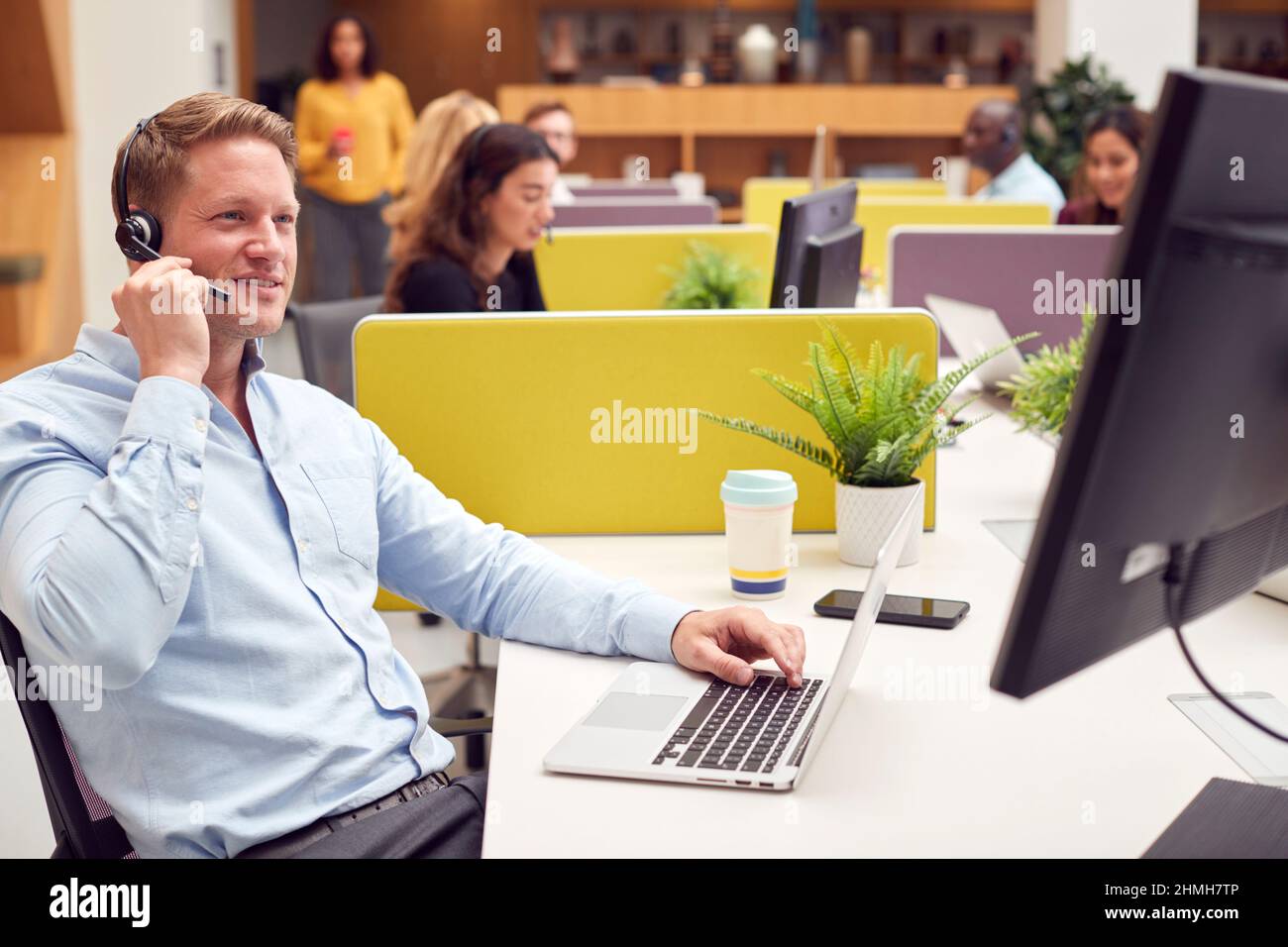Ein Geschäftsmann Mit Headset Spricht Mit Dem Anrufer In Einem Geschäftigen Kundencenter Stockfoto