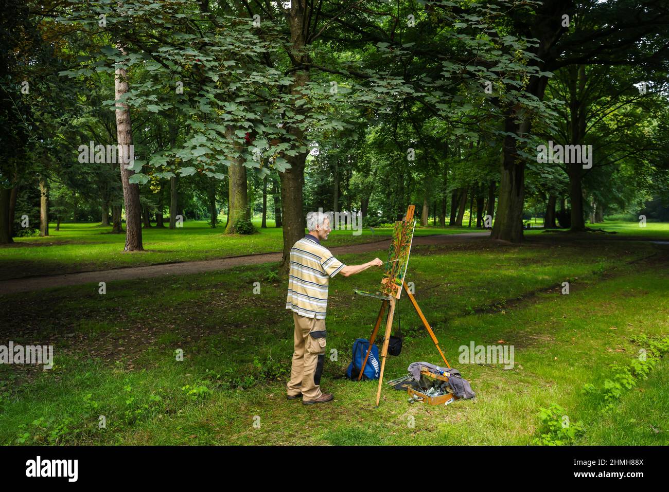 Marl, Nordrhein-Westfalen, Deutschland - Ein einheimischer Künstler malt im Friedenspark, dem alten Brassurfriedhof, ein Landschaftsbild auf eine Staffelei. Der alte Friedhof mit dem Skulpturenpark und den Skulpturen im öffentlichen Raum ist Teil der Außenanlagen des Skulpturenmuseums Glaskasten Stockfoto