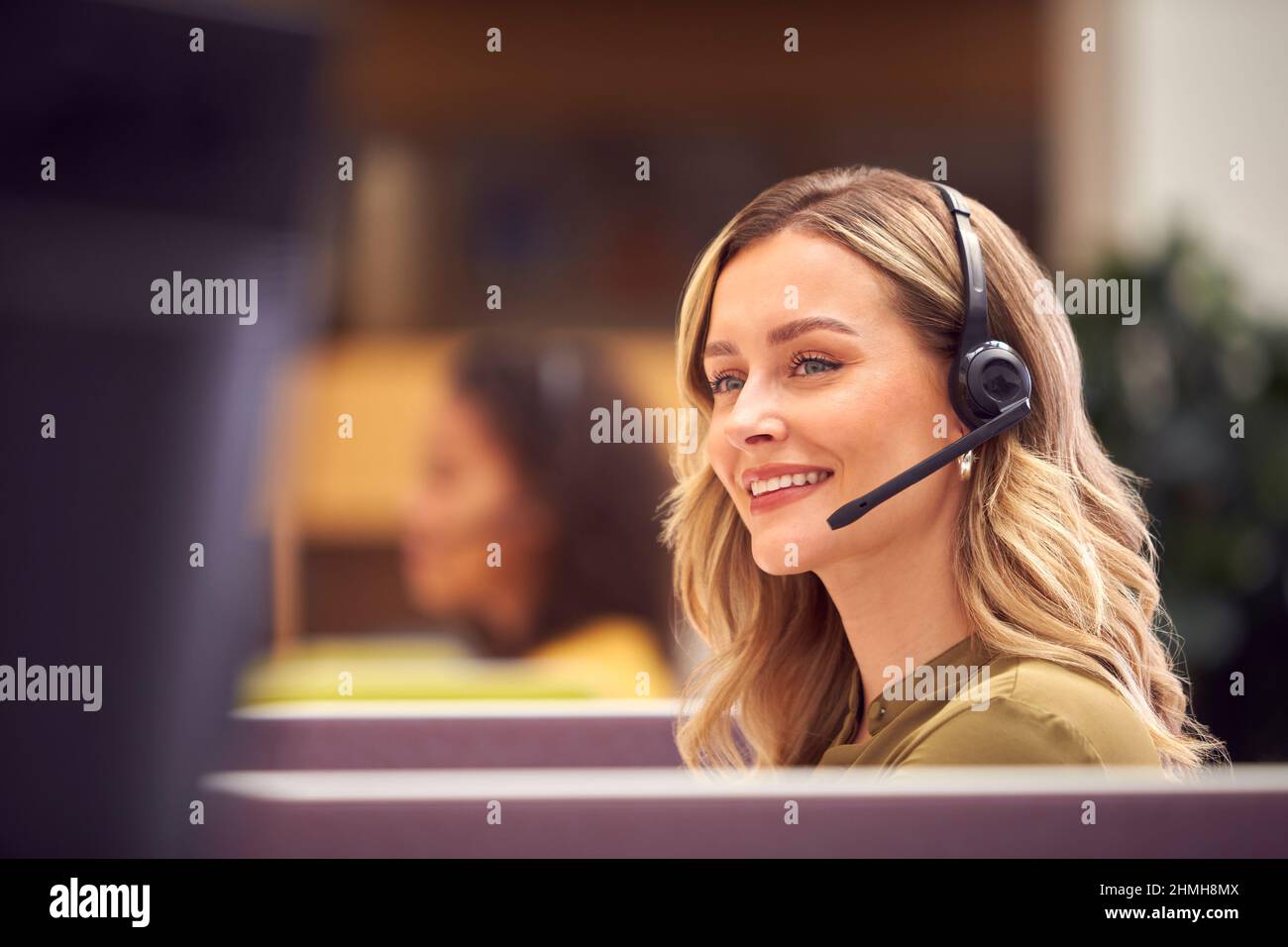 Eine Geschäftsfrau In Der Kabine Trägt Ein Headset Und Spricht Mit Dem Anrufer In Einem Stark Frequentierten Kundendienstzentrum Stockfoto