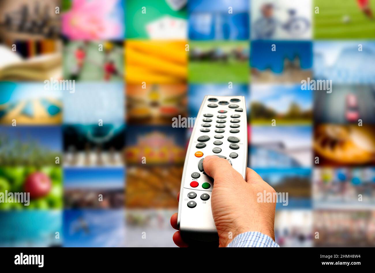 Hand mit Fernbedienung, die auf eine Wand aus Bildern, tv-Streaming und Multimedia-Konzept zeigt Stockfoto