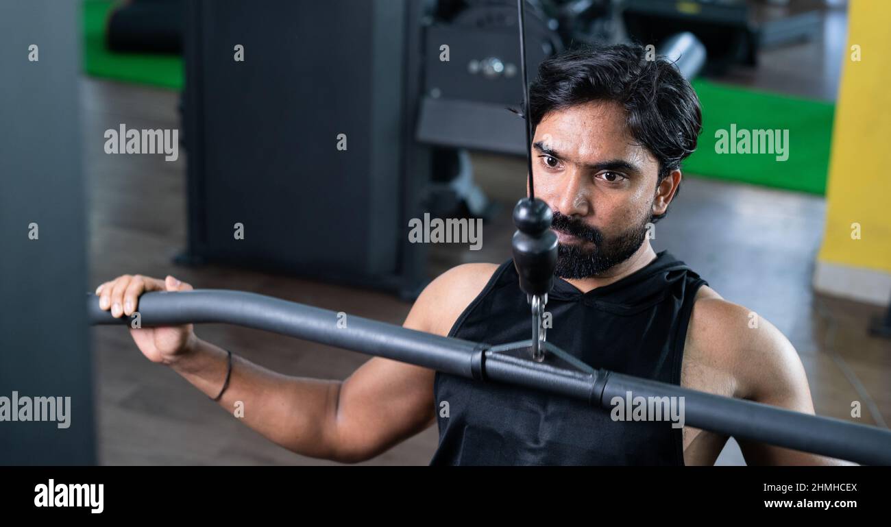 Junger Mann, der im Fitnessstudio mit seitlichem Zug trainiert – Konzept von Bodybuilding, gesunder Routine, fleißiger, inspirierender und sportlicher Lebensweise Stockfoto