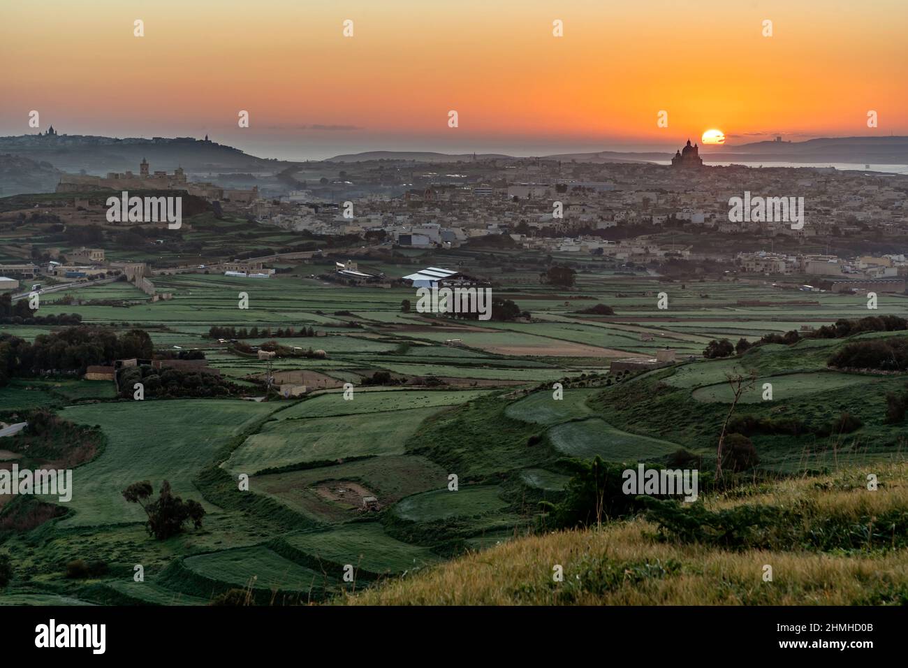 Am letzten Tag des Jahres geht die Morgensonne direkt hinter der Basilika in Goza, Malta, auf und taucht die Landschaft in goldenes Licht. Stockfoto