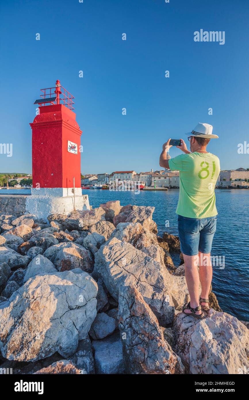 Kroatien, Kvarner Bucht, Insel Krk, Tourist, der einen Schnappschuss des roten Leuchtturms am Eingang zum Hafen von Krk macht Stockfoto