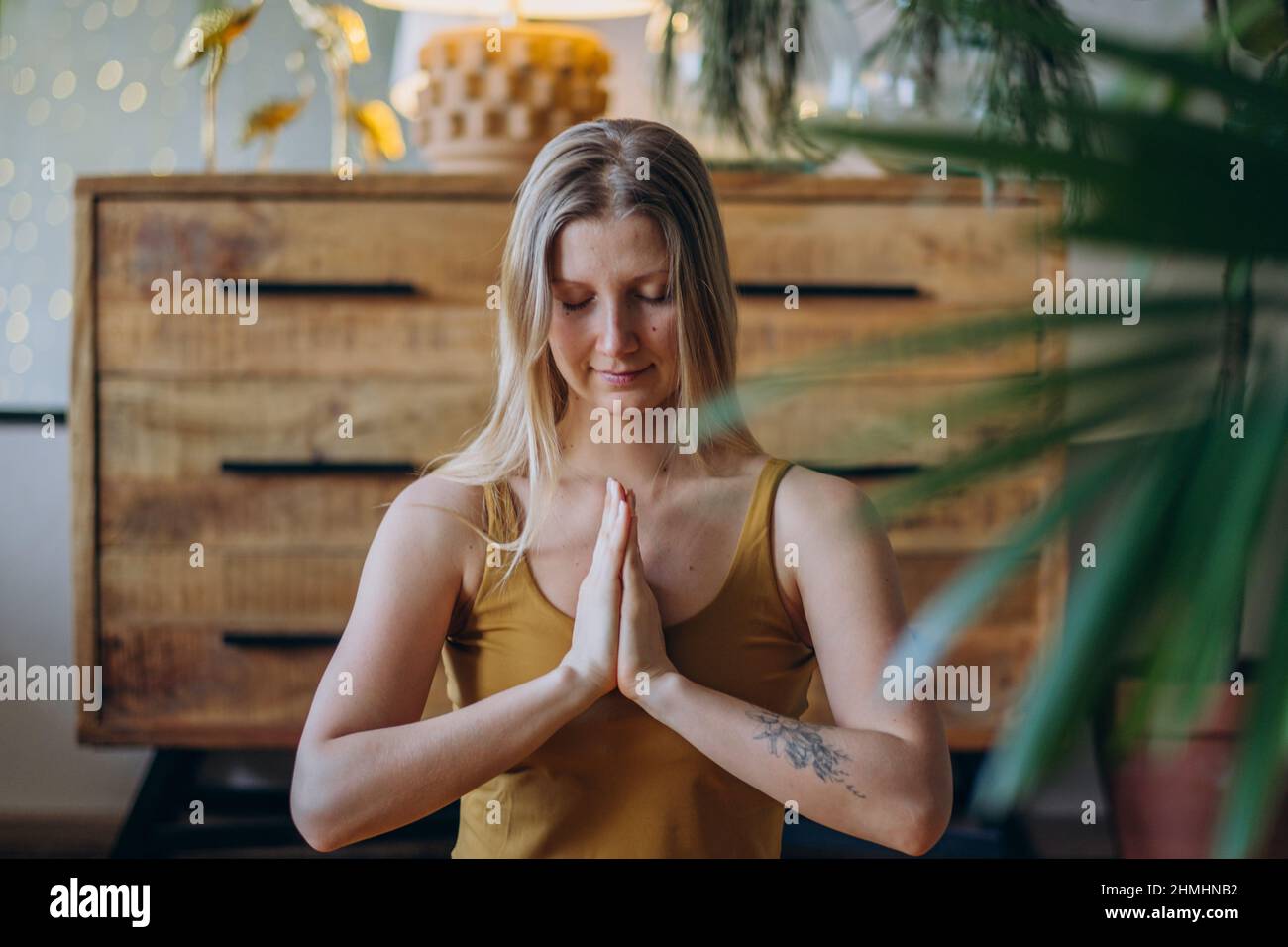 Eine athletische Frau mit blonden, lockeren Haaren und Tätowierungen in der Oberseite und Leggings meditiert mit einem breiten Lächeln in Lotushaltung auf der Yoga-Matte aus der Nähe Stockfoto