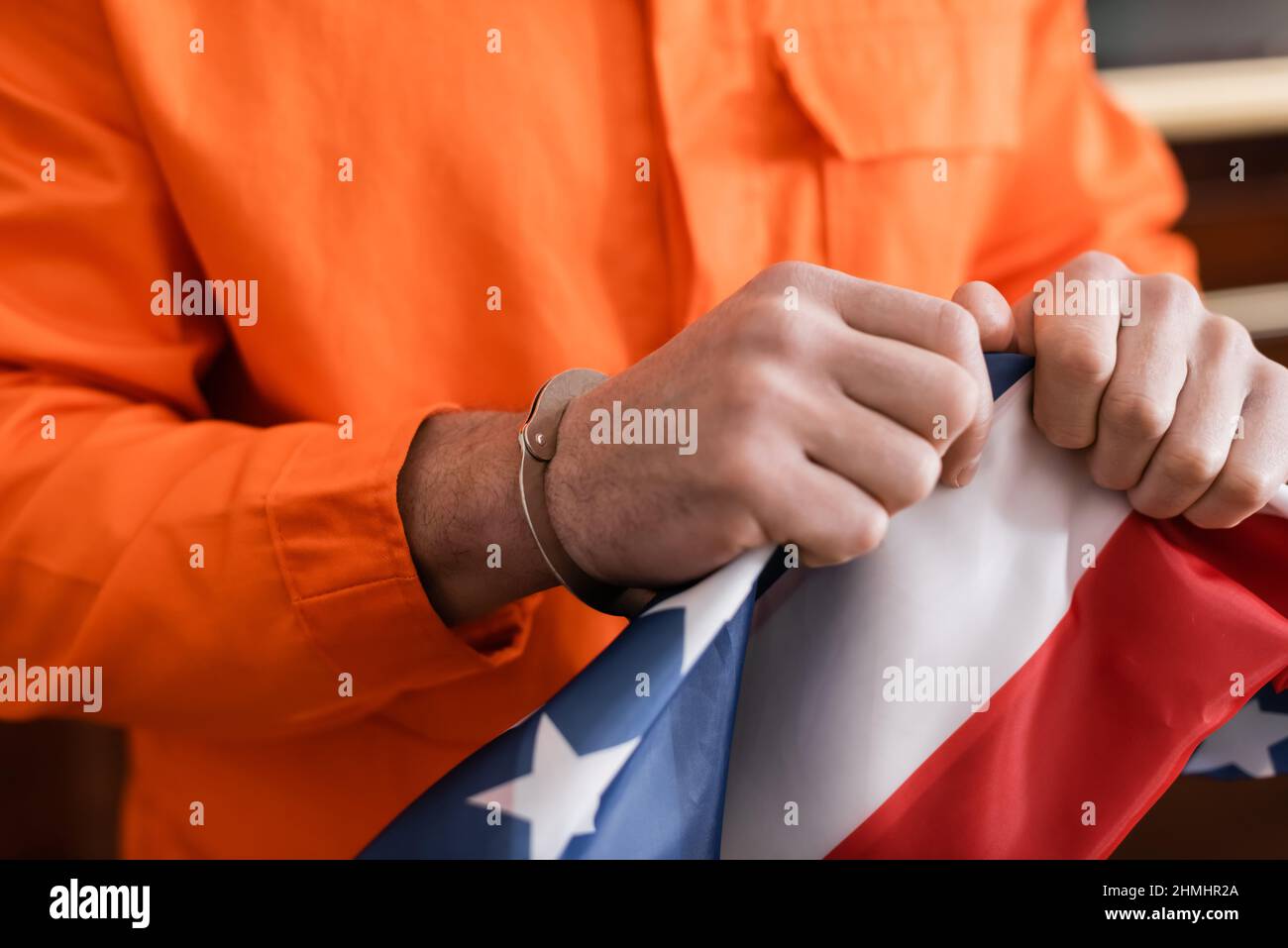Teilansicht eines verurteilten Mannes in Handschellen und einer Gefängnisuniform, die die us-Flagge zerreißt, Justizkonzept Stockfoto