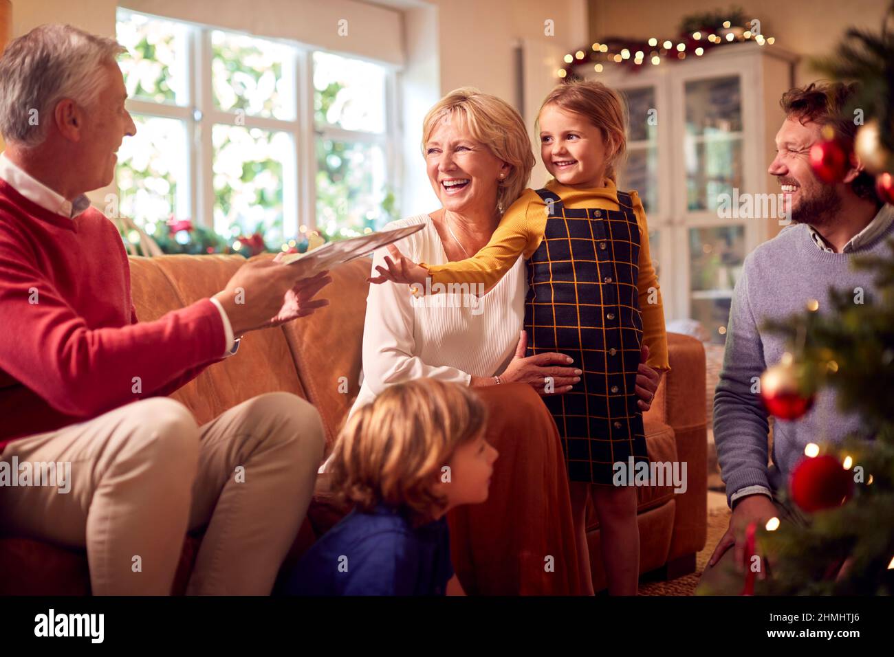 Enkelin Verteilt Geschenke An Die Familie Mehrerer Generationen Um Den Weihnachtsbaum Zu Hause Stockfoto