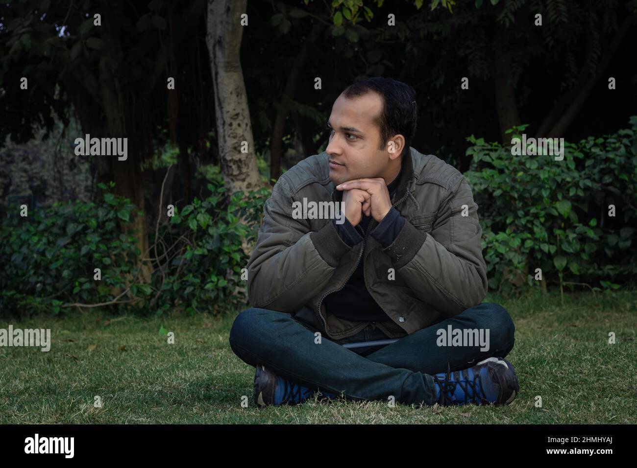 Junger Mann verschiedene Stimmungen des Ausdrucks Kreuz Bein sitzt in einem Park aus flachem Winkel Stockfoto