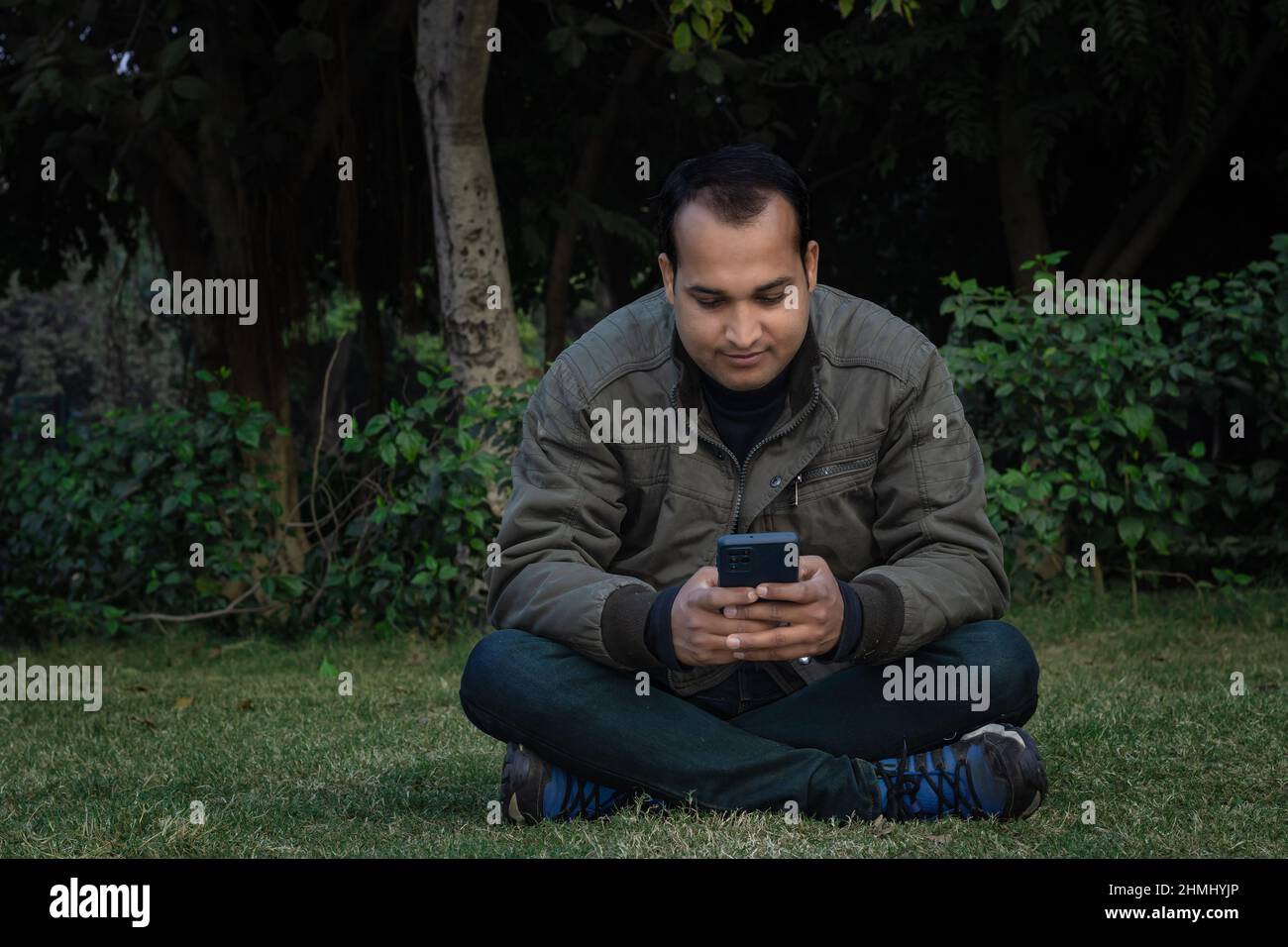 Junger Mann verschiedene Stimmungen des Ausdrucks Kreuz Bein sitzt in einem Park aus flachem Winkel Stockfoto