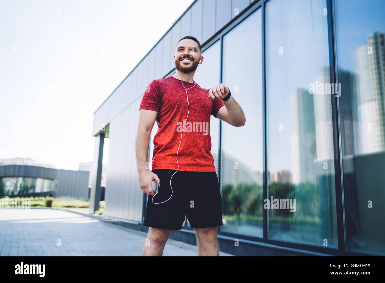 Fröhlicher Sportler, der mit Kopfhörern auf der Straße steht Stockfoto