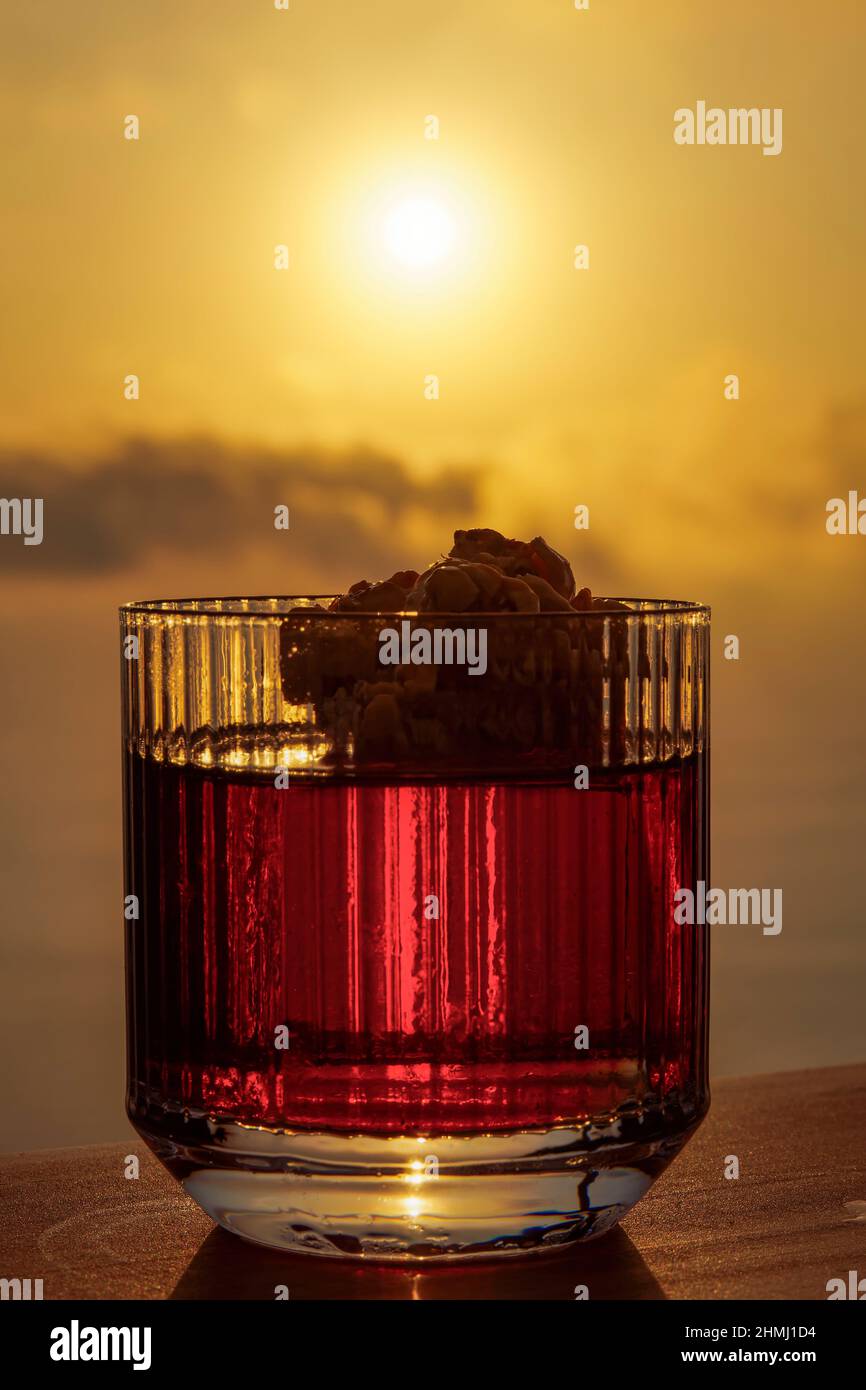 Negroni-Cocktail in einem altmodischen, garnierten Glas vor orangefarbenem Sonnenuntergang. Italienischer alkoholischer Aperitivo vor entkochten gelben Himmel backgrοund. Stockfoto