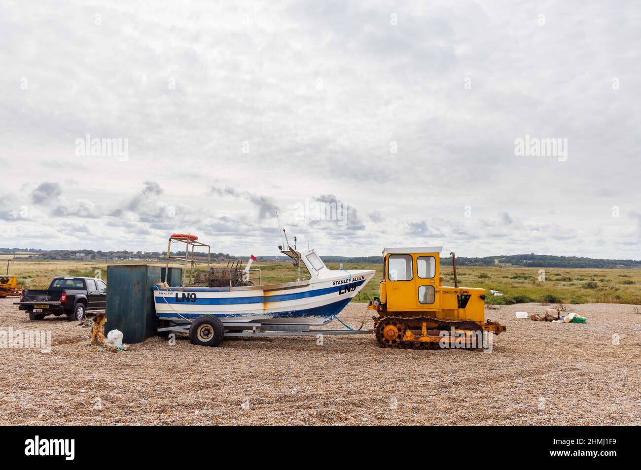 Fischerboot auf einem Anhänger, der von einem Raupendozer auf einem Kiesstrand, Cley-Next-the-Sea, einem Küstendorf in Norfolk, East Anglia, England, gezogen wird Stockfoto