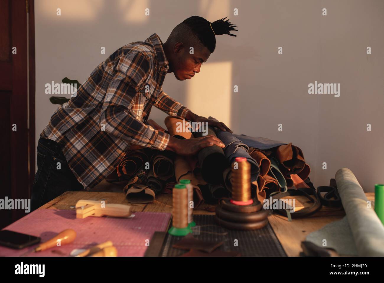 Seitenansicht eines afroamerikanischen jungen Handwerkers, der in der Werkstatt Leder auf der Werkbank auswählt Stockfoto