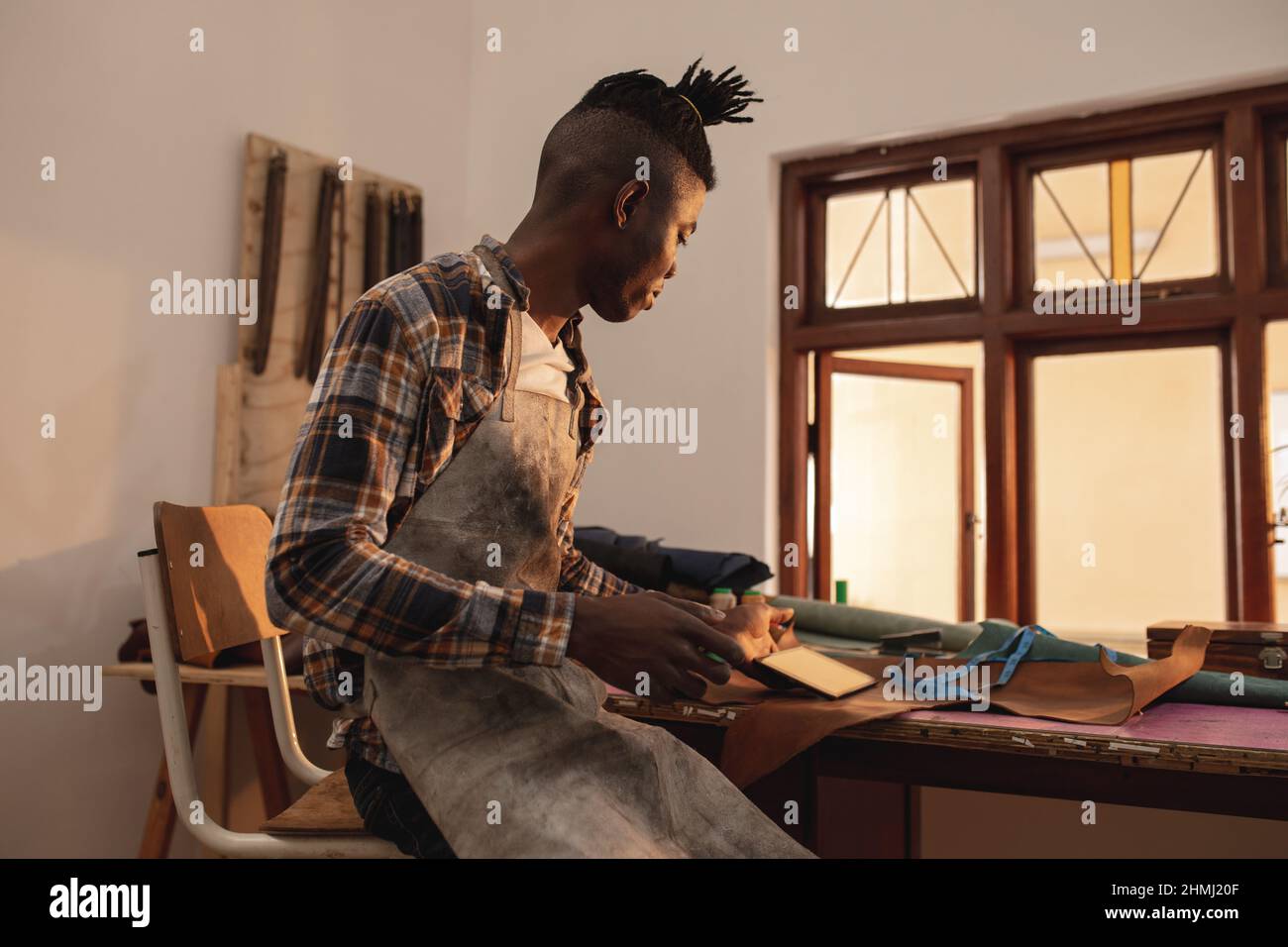 afroamerikanischer junger Handwerker mit digitalem Tablet während der Arbeit in einer Lederwerkstatt Stockfoto