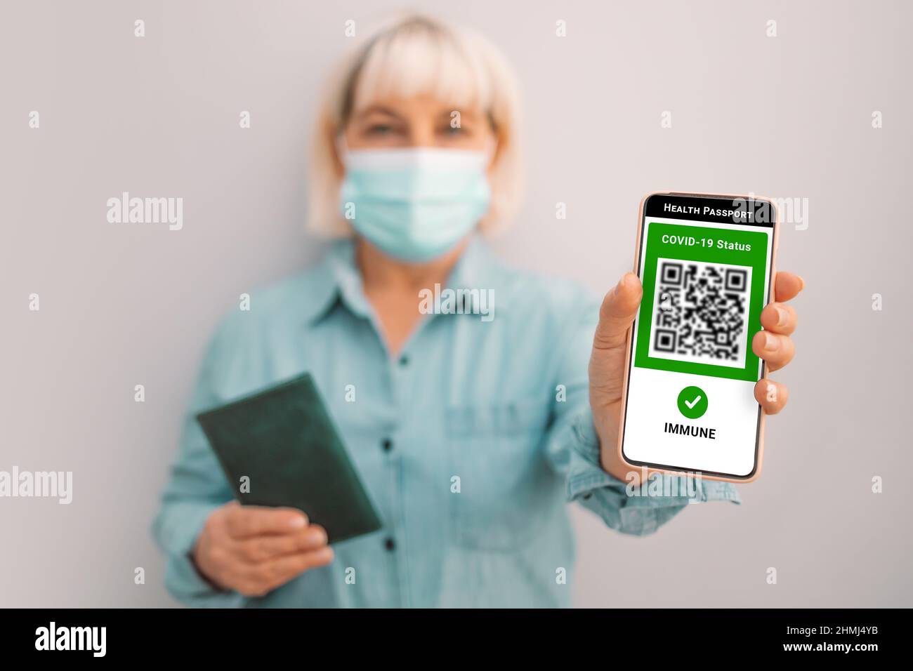 Covid-19-Steuerung. 50s kaukasische Frau in Maske hält Smartphone mit digitalem grünen Pass und QR-Code auf dem Bildschirm. Gesundheitspass oder Bescheinigung von Stockfoto