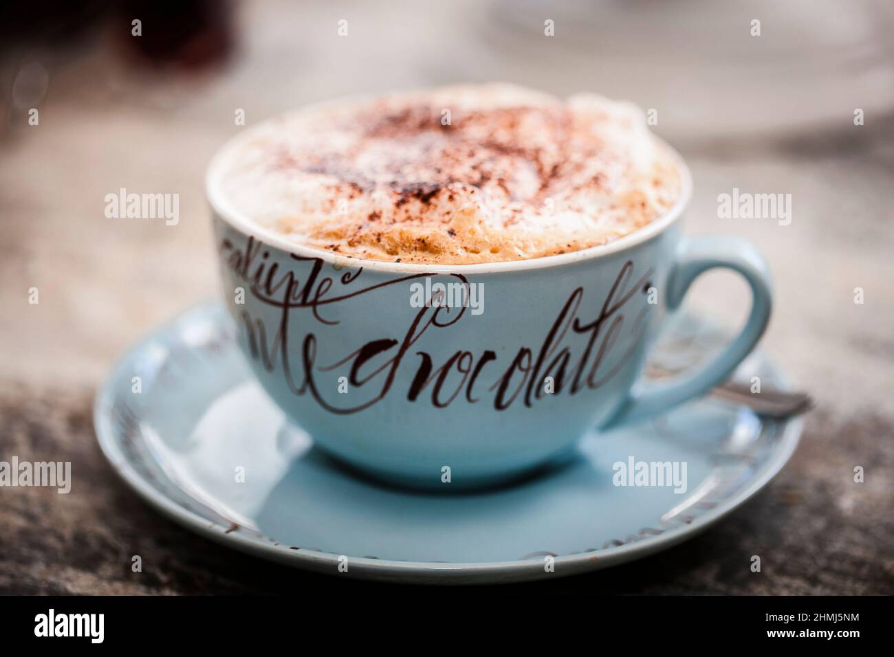 Heiße Schokolade mit einer Prise Kakaopulver in einem dekorativen Becher auf einer rustikalen Holzarbeitsfläche Stockfoto