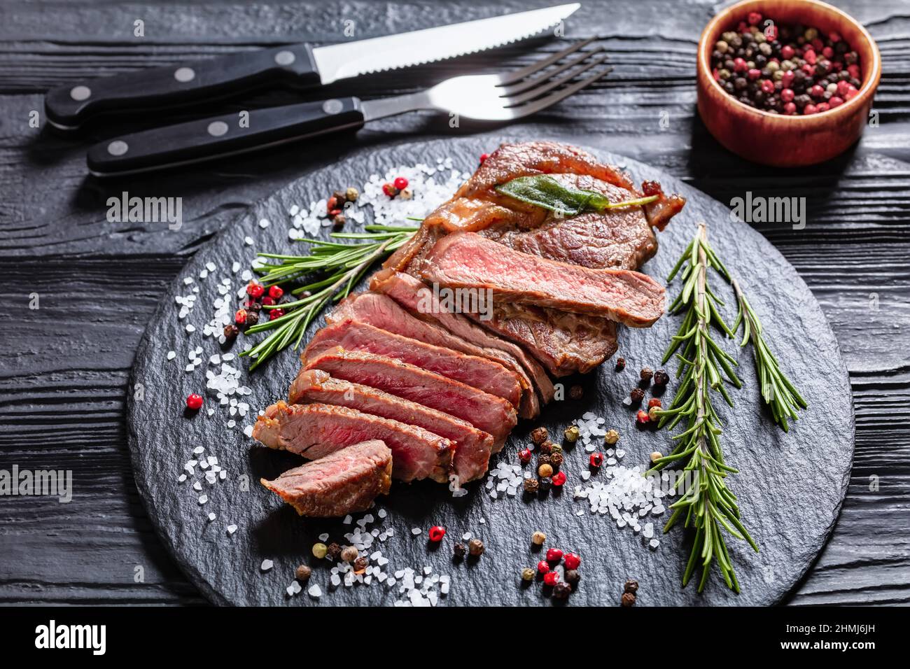 Röststeak auf schwarzem Schiefer mit Rosmarin, Salz und Pfefferkörnern, Draufsicht, Nahaufnahme Stockfoto