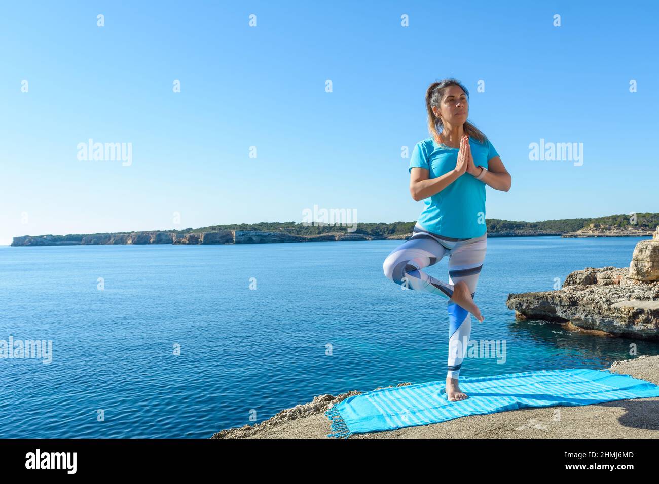 Fitness-Frau mittleren Alters im Freien vor dem Meer macht Yoga-Stretching-Übungen. Stockfoto