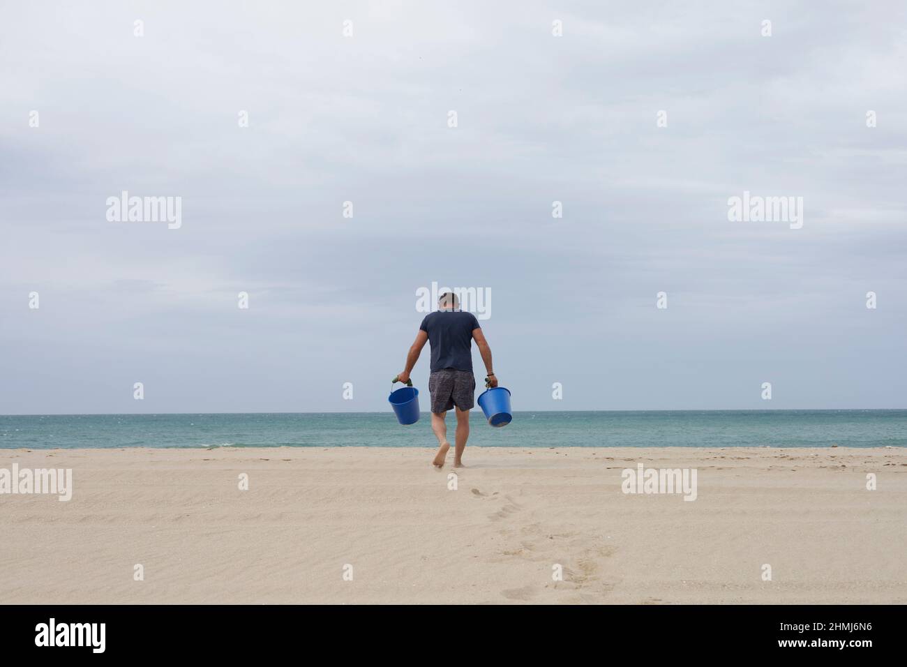 Ein Mann mit zwei Eimern am Victoria Beach in Cadaz, Spanien. Stockfoto
