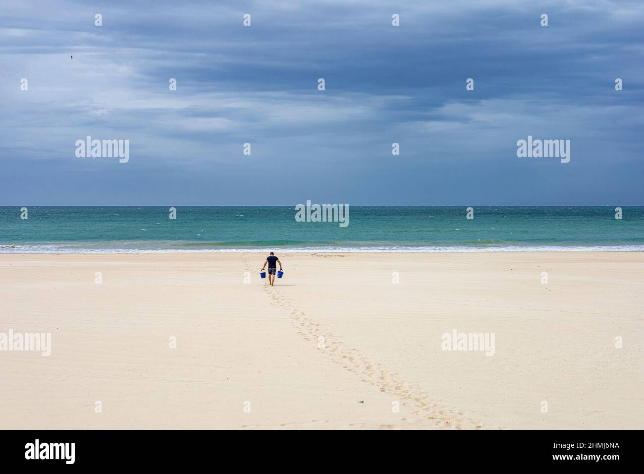 Ein Mann mit zwei Eimern am Victoria Beach in Cadaz, Spanien. Stockfoto