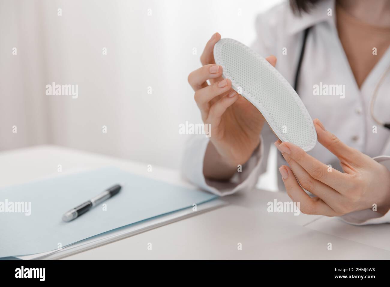 Arzt, der eine Einlegesohle hält, während er an einem Tisch sitzt. Orthopäde testet das medizinische Gerät. Orthopädische Einlagen. Fußpflege. Korrektur Der Flachen Füße Stockfoto