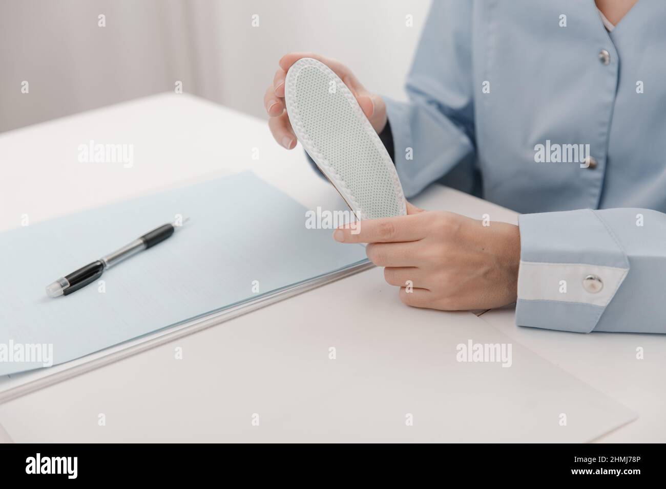 Arzt, der eine Einlegesohle hält, während er an einem Tisch sitzt. Orthopäde testet das medizinische Gerät. Orthopädische Einlagen. Fußpflege. Korrektur Der Flachen Füße Stockfoto