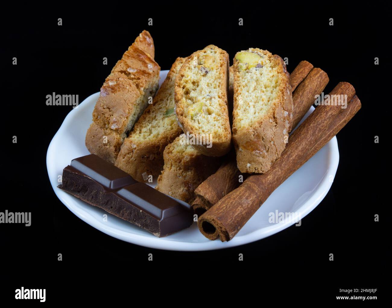 Cinnanon-Sticks, Schokolade und Bisquits in einem weißen Teller isoliert auf schwarzem Hintergrund Stockfoto