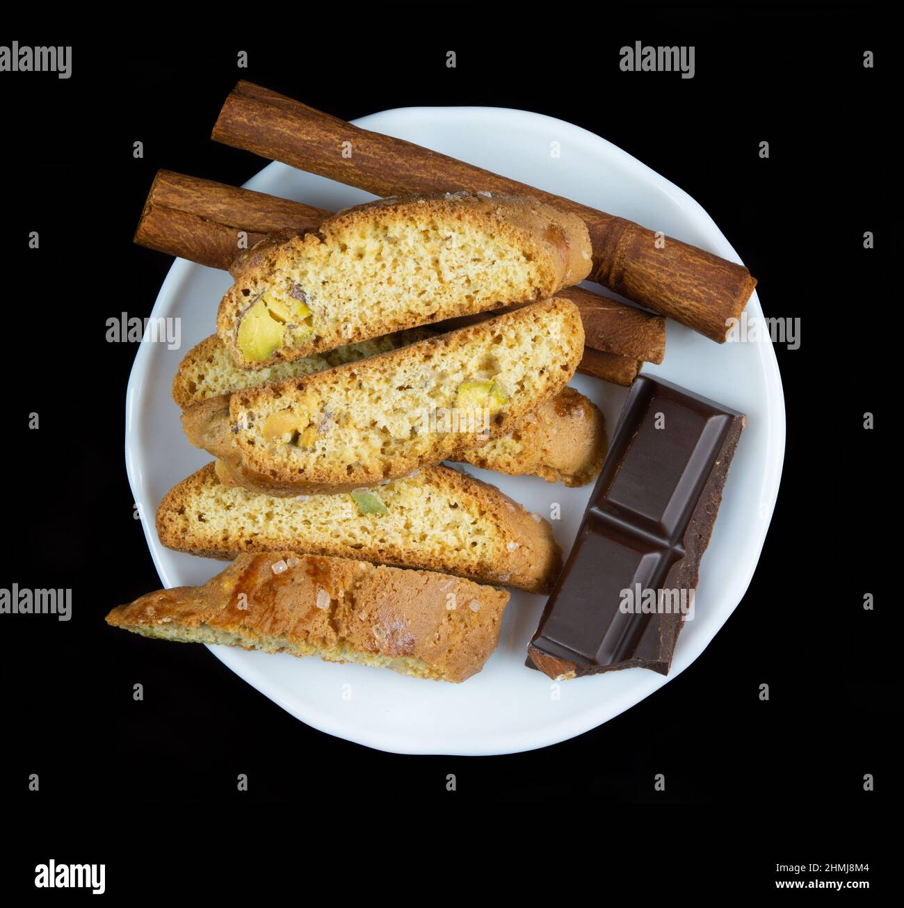 Cinnanon-Sticks, Schokolade und Bisquits in einem weißen Teller isoliert auf schwarzem Hintergrund Stockfoto