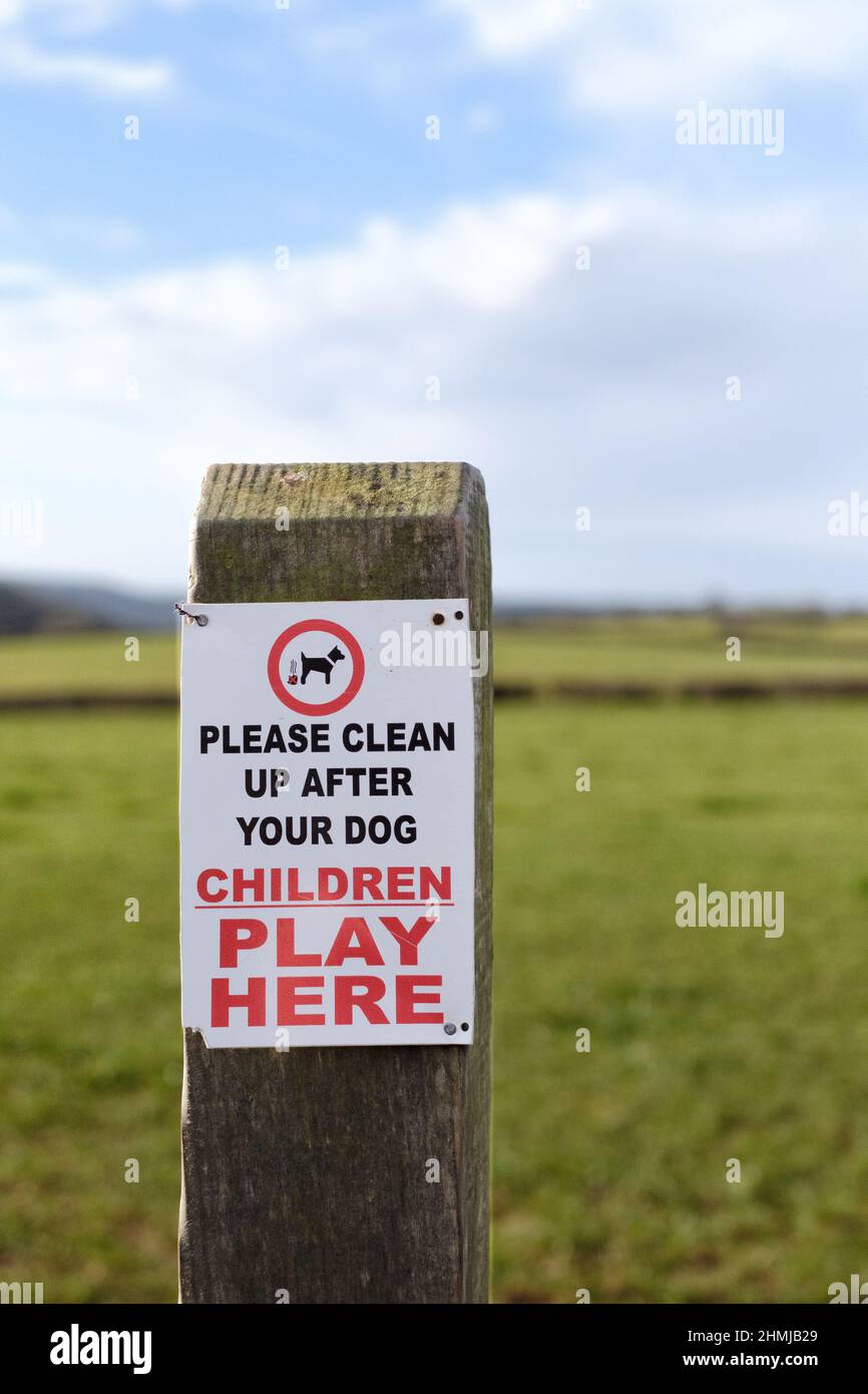 Ein Schild, das an einem Pfosten befestigt ist und Hundebesitzer und Hundespaziergänger auffordert, jegliches Chaos zu beseitigen oder ihre Hunde zu bescheuern, kann in einem Bereich, in dem Kinder spielen, auftreten. Stockfoto