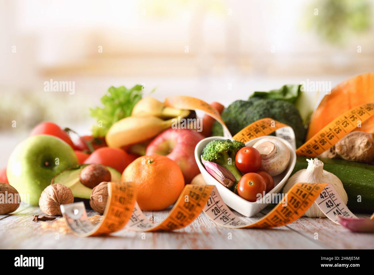 Gesunde und diätetische Lebensmittel mit Obst und Gemüse auf Küchenbank mit herzförmiger Schüssel und Maßband. Vorderansicht. Horizontale Zusammensetzung. Stockfoto