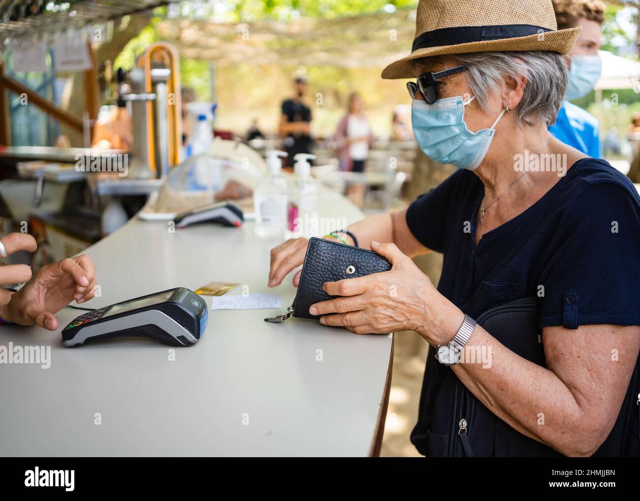 Eine ältere Dame, die kontaktlos an der Bar eines Cafés außerhalb des Cafés bezahlt, trägt eine Gesichtsmask, um sie vor Covid-19 zu schützen Stockfoto
