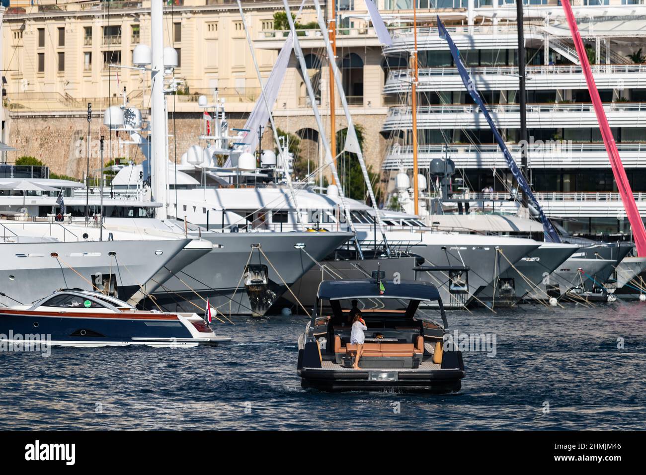 Ein großes Boot fährt in den Hafen, das Mädchen auf dem Deck telefoniert, viele riesige Yachten befinden sich im Hafen von Monaco im Hintergrund, Monte Carlo Stockfoto