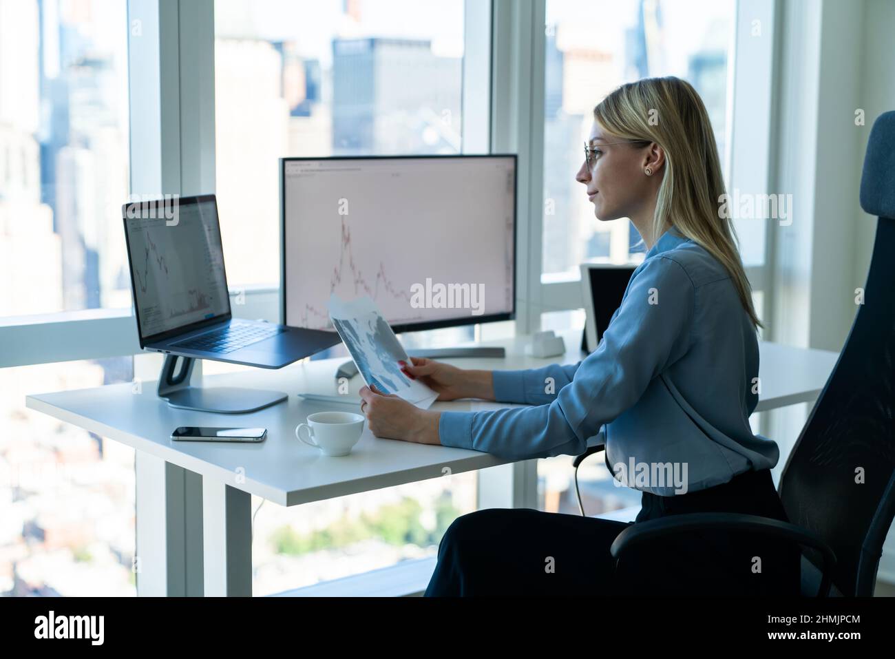 Positive Geschäftsfrau, die im Büro an einem Laptop und einem Computermonitor arbeitet Stockfoto