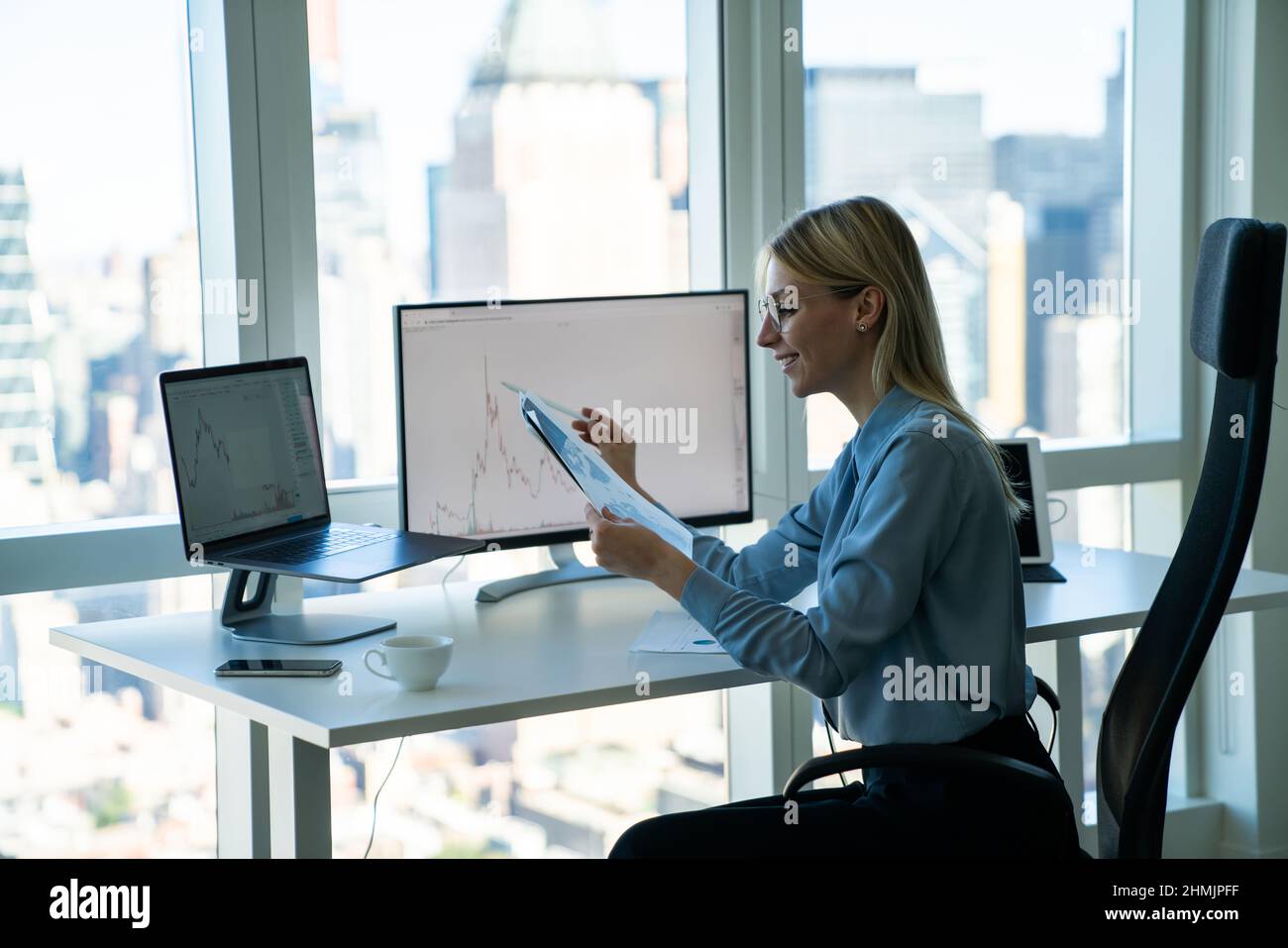 Fröhliche Geschäftsfrau, die im modernen Büro mit Gadgets am Schreibtisch arbeitet Stockfoto