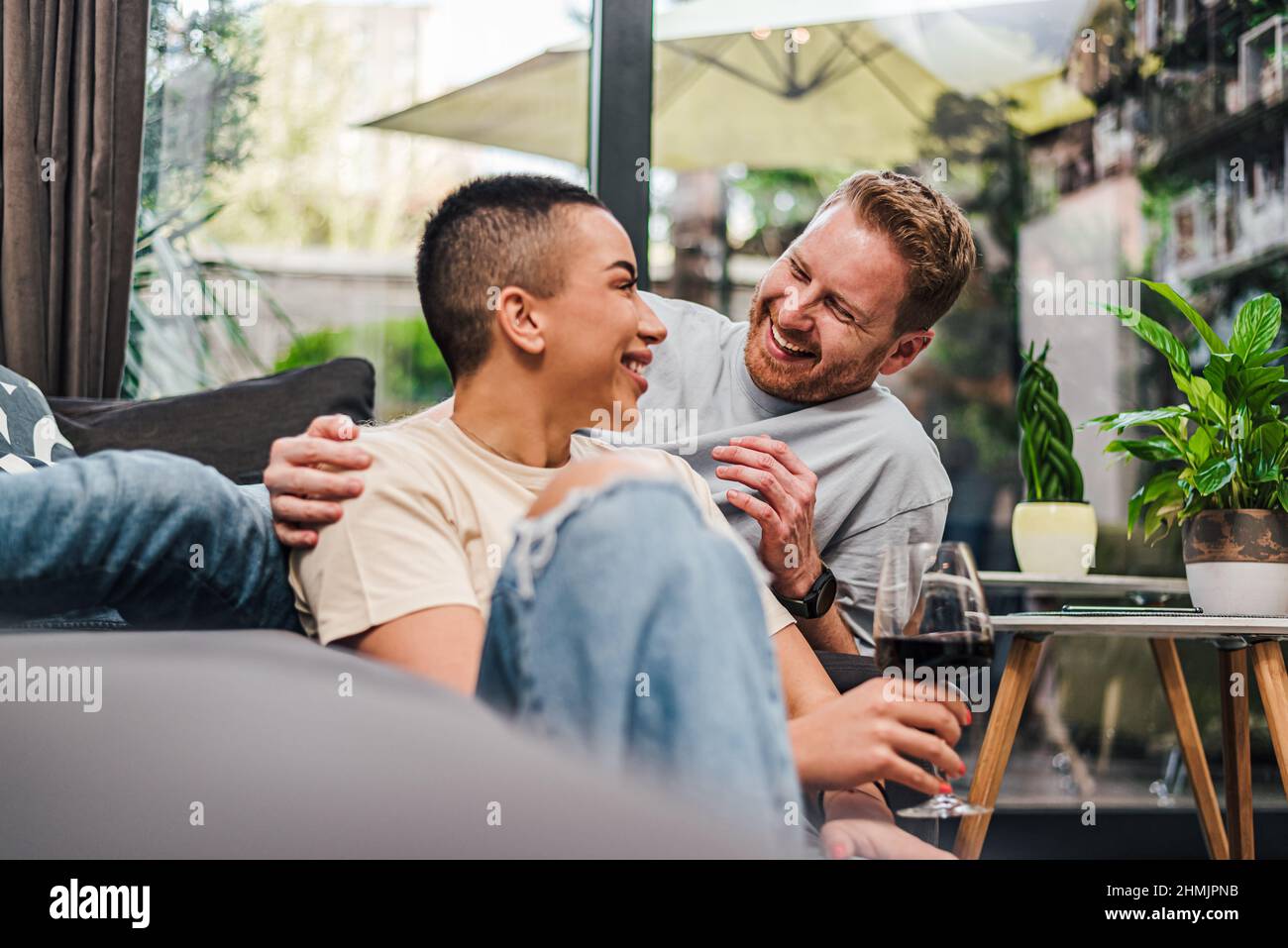 Junge Erwachsene Personen Paar genießen sich und haben eine tolle Zeit zu Hause zwanglose Atmosphäre trinken Wein lächelnd Lachen glücklich Gefühle Freude entspannen Stockfoto